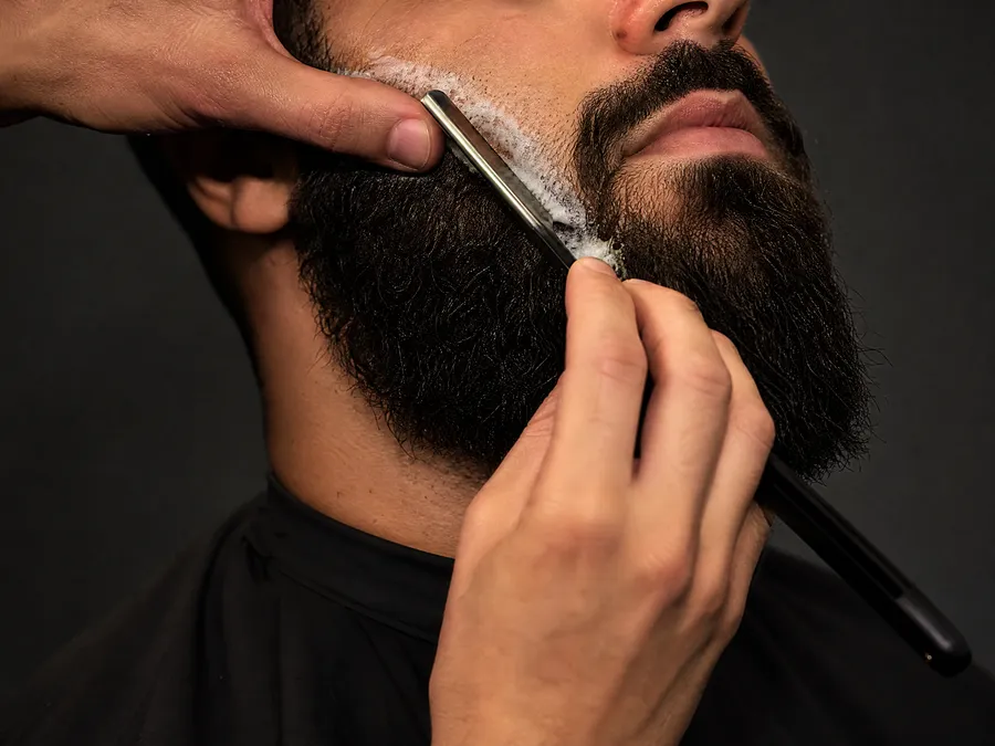 Navalha contornando uma barba cheia.